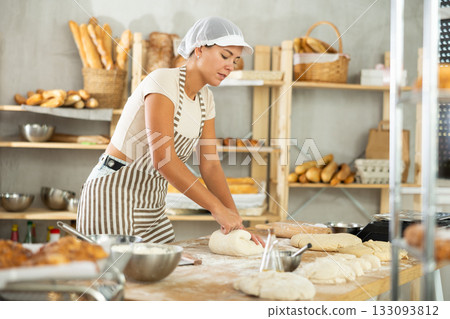 Young woman works in bakery as baker, kneads and prepare dough, works with flour. 133093812