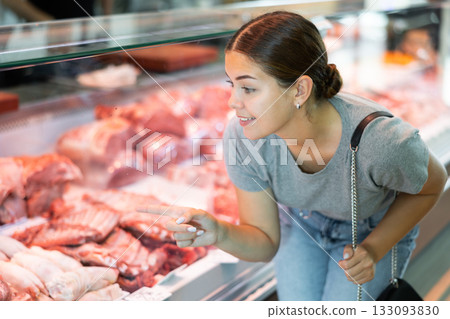 Young woman buyer chooses pork in butcher shop 133093830