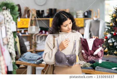 Latina chooses a bra against the background of a Christmas tree in a store Latina chooses a bra against the background of a Christmas tree in a store 133093837