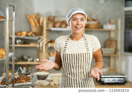 Young baker girl is standing near work table in kitchen, working with dough 133093859