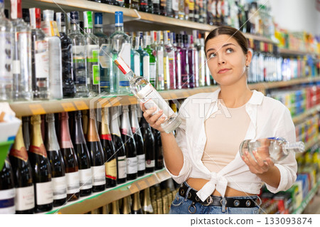 in hard liquor department, young woman carefully chooses vodka 133093874