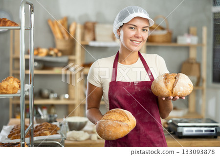 Young woman are standing in kitchen with finished products two loaves of rye bread Young woman are standing in kitchen with finished products two loaves of rye bread 133093878