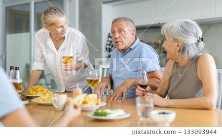 Old men and women talking merrily while having snack in the kitchen Old men and women talking merrily while having snack in the kitchen 133093944