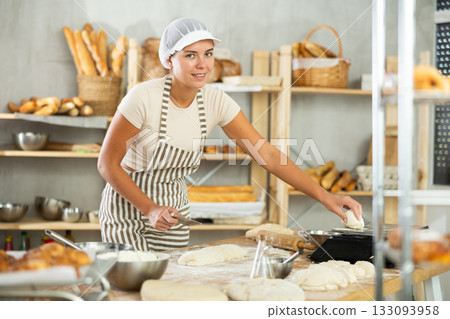 Girl baker cut small pieces of dough from large lump and put them on scales. 133093958