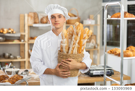 Young male baker holding baguettes in round wicker basket Young male baker holding baguettes in round wicker basket 133093969