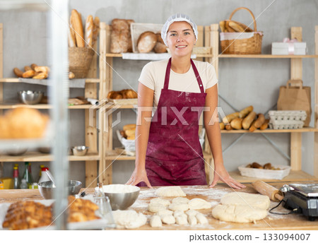 Smiling young female baker pausing during kneading dough in bakery Smiling young female baker pausing during kneading dough in bakery 133094007