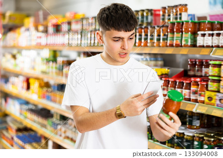 Guy scanning barcode on jar of canned food with phone in supermarket Guy scanning barcode on jar of canned food with phone in supermarket 133094008