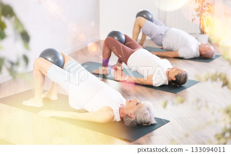 Lady does lightweight bridge pose - Setu Bandhasana and holds softball in lap. Lady does lightweight bridge pose - Setu Bandhasana and holds softball in lap. 133094011