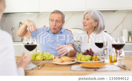 Mature married couple with female friend are sitting at table, enjoying food and wine, chatting. 133094012