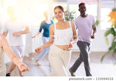 Young teacher and group of positive aged people engaged in dynamic dances 133094018