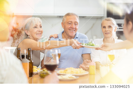 Happy carefree older man and women gathering around kitchen table 133094025