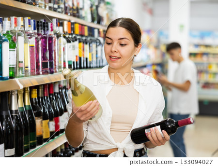 Smiling young girl choosing alcoholic beverages in store 133094027