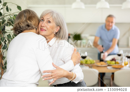 Two elderly woman greet each other by kissing each other on the cheek. While men shake hands 133094028