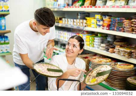 in supermarket in department of semi-finished products, couple chooses pizza 133094032
