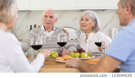 Two mature married couples are sitting at table, enjoying food and wine, chatting. Two mature married couples are sitting at table, enjoying food and wine, chatting. 133094039