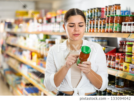 Pensive young girl choosing canned goods in supermarket 133094042