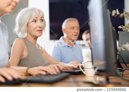 Portrait of an elderly positive woman working on computer with group of friends while attending PC classes in nursing home Portrait of an elderly positive woman working on computer with group of friends while attending PC classes in nursing home 133094060