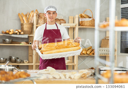 Happy male baker posing with basket of freshly baked baguettes in bakery, demonstrating concept of food industry and baker profession Happy male baker posing with basket of freshly baked baguettes in bakery, demonstrating concept of food industry and baker profession 133094061