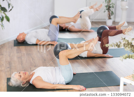 People lying on karemat, pulled bent legs to themselves and clamped soft-ball in knee 133094072