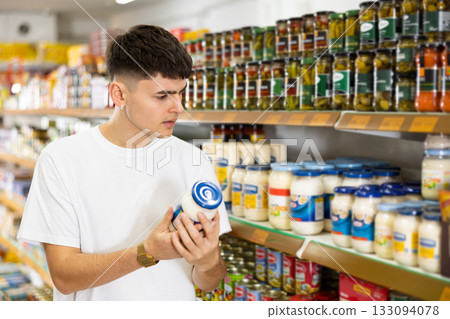 Young male customer diligently picking out jar of mayonnaise 133094078