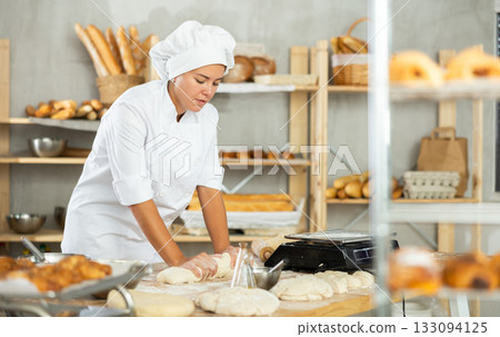 Young woman works as baker, mold baguette from dough, creates long loafs from dough. 133094125