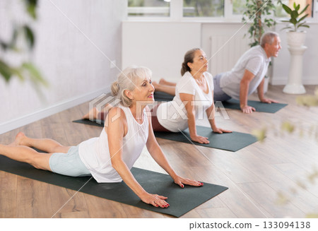 Elderly women practicing yoga in virabhadrasana pose in gym 133094138