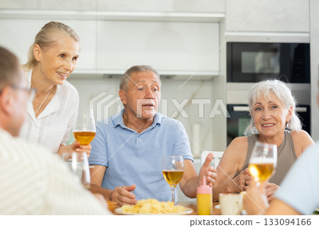 Joyful elderly women and man chatting and drinking at kitchen table 133094166
