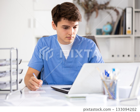 Male doctor working in a clinic typing patient treatment appointment record on a laptop in office Male doctor working in a clinic typing patient treatment appointment record on a laptop in office 133094202
