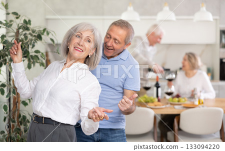 Senior man and woman doing couple dancing with their backs to each other during house party. 133094220