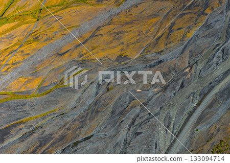 Aerial view of Icelandic landscape with braided river channels, vibrant yellow and green moss, and dark sediment patterns shaped by volcanic activity. 133094714