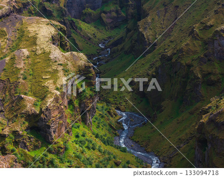 Mulagljufur Canyon in Iceland features steep moss covered cliffs and a winding river. Soft natural light highlights the vibrant greenery and rugged terrain. Mulagljufur Canyon in Iceland features steep moss covered cliffs and a winding river. Soft natural light highlights the vibrant greenery and rugged terrain. 133094718