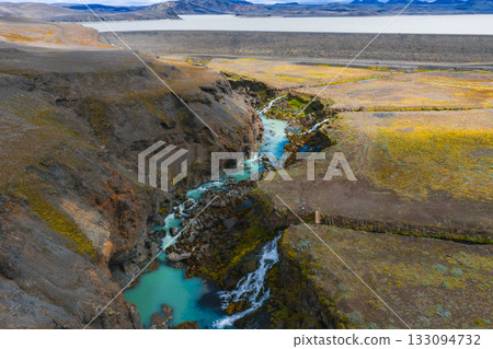 A turquoise river winds through Sigoldugljufur Canyon in Iceland, with moss covered cliffs, a small waterfall, a distant lake, and mountains visible. A turquoise river winds through Sigoldugljufur Canyon in Iceland, with moss covered cliffs, a small waterfall, a distant lake, and mountains visible. 133094732