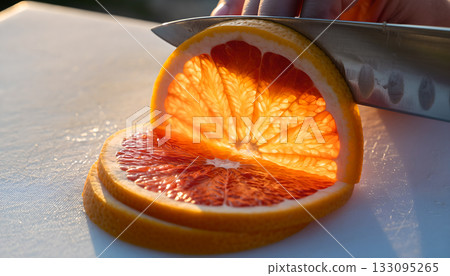 Knife slicing through bright grapefruit segments on light surface showcasing citrus preparation 133095265