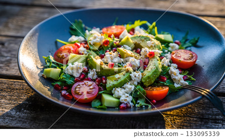 A vibrant salad showcasing fresh avocado, ripe tomatoes, and creamy feta on rustic wood surface 133095339