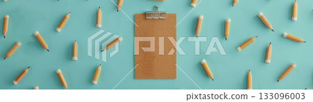 A clipboard surrounded by pencils on a vibrant blue surface, ideal for educational or creative projects. 133096003