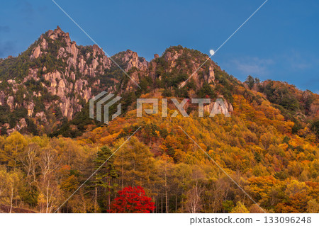 The moon rising over Mt. Mizugaki and autumn leaves in the evening from Mizugaki Natural Park in autumn The moon rising over Mt. Mizugaki and autumn leaves in the evening from Mizugaki Natural Park in autumn 133096248