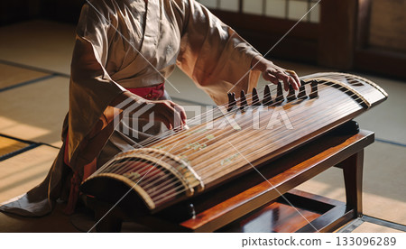 Elegant kimino clad woman plays traditional japanese koto creating tranquil melody in sunlit zen 133096289