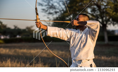 Focused archer drawing bow in traditional kyudo practice under soft sunlight a moment of 133096293