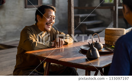 A smiling asian man sharing stories over tea in a rustic rural setting atmosphere with an intimate 133097197