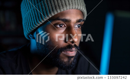 Focused programmer with thoughtful expression illuminated by screen in dim setting creating a 133097242