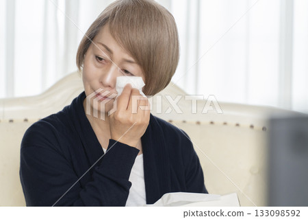 Senior woman crying while watching sad TV in the living room 133098592