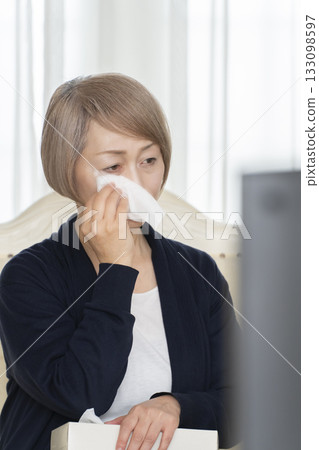 一位老婦人在客廳一邊看悲傷的電視節目一邊哭泣 133098597