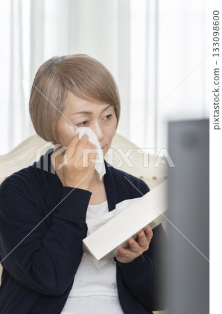 一位老婦人在客廳一邊看悲傷的電視節目一邊哭泣 一位老婦人在客廳一邊看悲傷的電視節目一邊哭泣 133098600