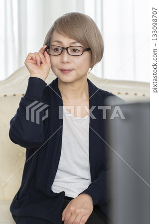 Senior woman wearing glasses watching TV in the living room Senior woman wearing glasses watching TV in the living room 133098707
