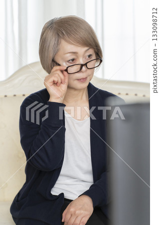 一位戴著眼鏡的老婦人在客廳看電視 一位戴著眼鏡的老婦人在客廳看電視 133098712