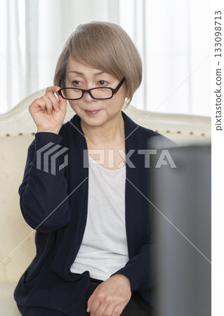 Senior woman wearing glasses watching TV in the living room Senior woman wearing glasses watching TV in the living room 133098713
