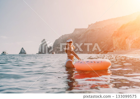 Woman, beach, ocean. Young woman in white bikini stands with donut float enjoying a sunny summer vacation. 133099575
