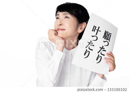 一位老婦人面帶微笑，手裡拿著一張紙，上面寫著「我的願望實現了」。她手托著下巴。 133100102