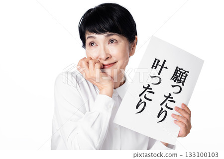 一位身穿白襯衫的老婦人手裡拿著一張紙，上面寫著“我的願望實現了”，臉上帶著意味深長的微笑。 133100103