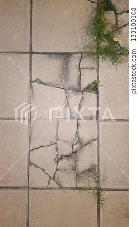 Cracked concrete tile floor, broken pavement, damaged surface, urban decay, rough texture, green grass, gritty mood 133100108